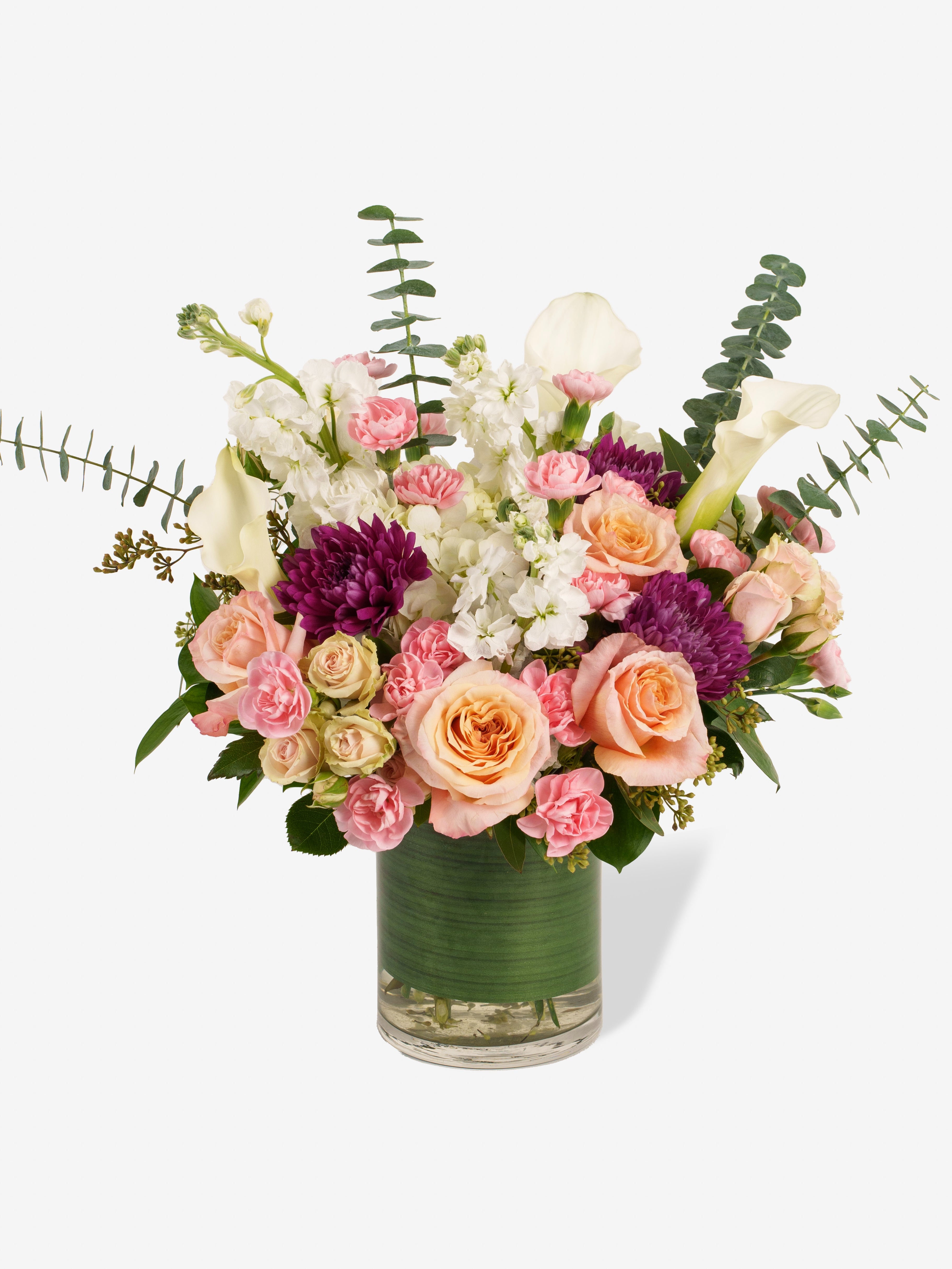 Bouquet of flowers in a clear vase on a white background with Calla Lilies, Roses, Carnations and Stock